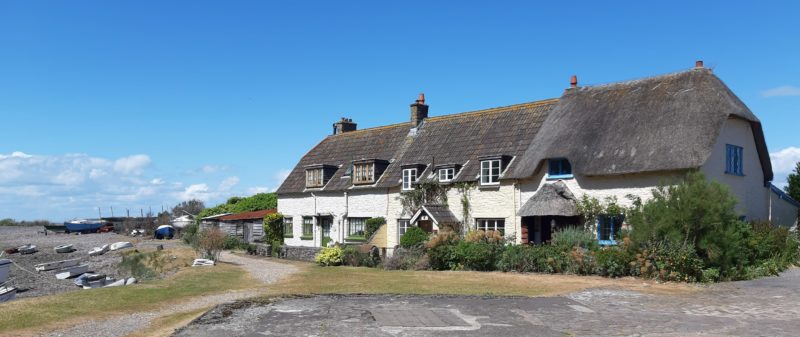 Row of picturesque cottages by the shingle on Porlock Weir, built of rubble stone and colour-washed. One retaining original