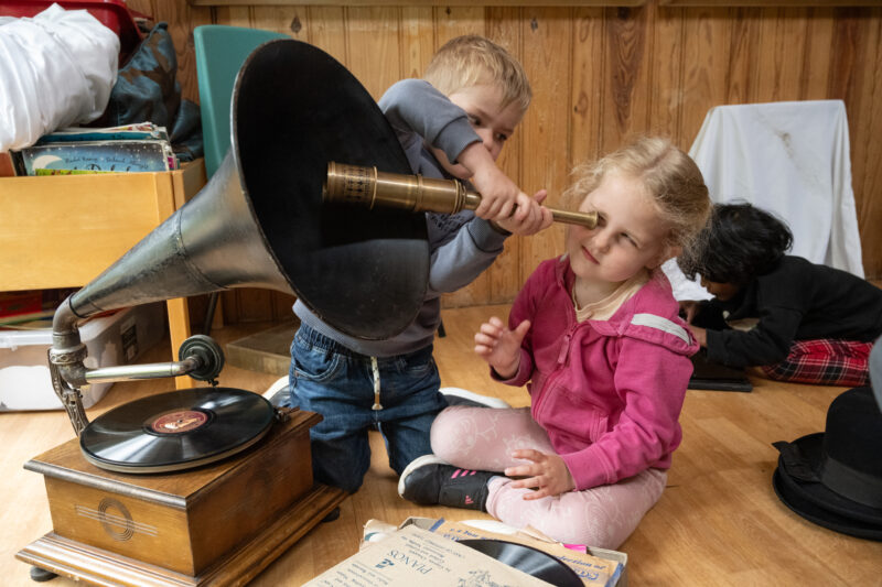 Two children playing with a vintage telescope sat in front of a gramophone.