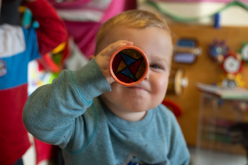 Child looking through a vintage toy towards the camera.