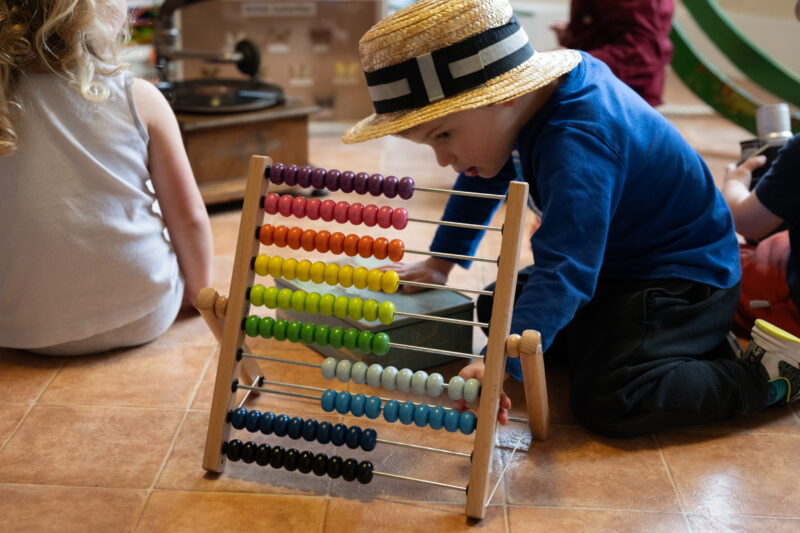 Child wearing a hat playing near a toy abacus.