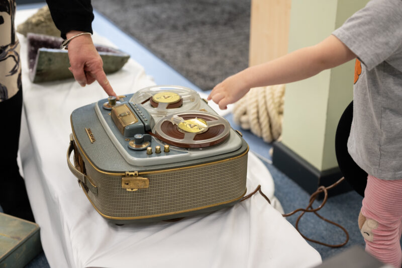 Child touching a vintage reel-to-reel tape recorder.