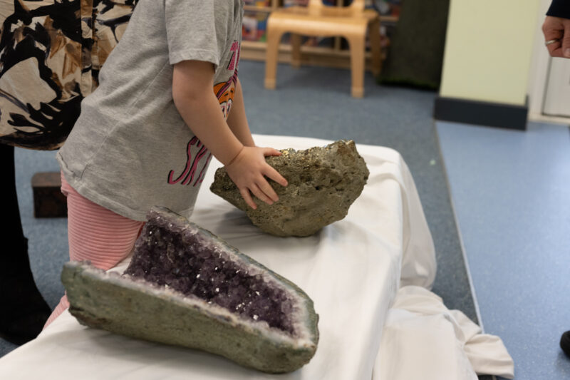 Child touching a large lump of fools gold with large amethyst in foreground.