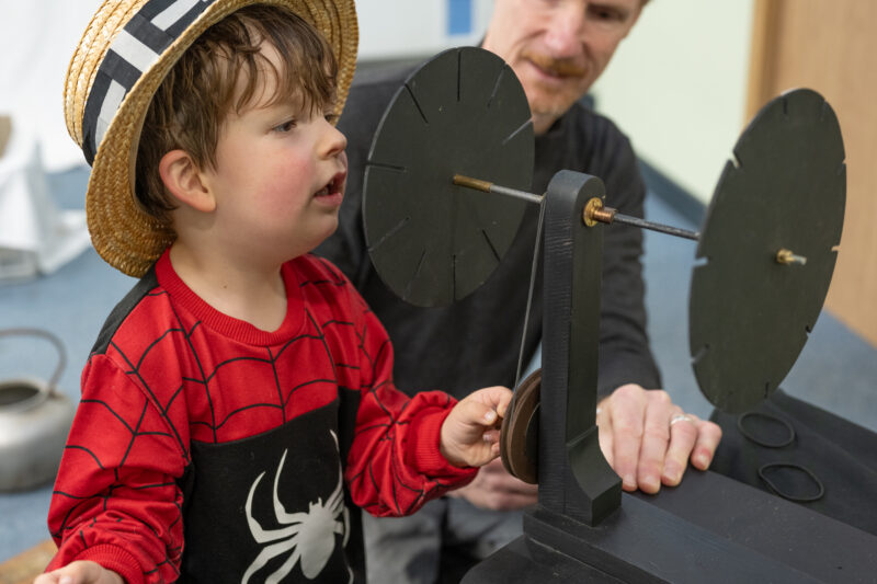 Child wearing a hat and looking through and playing with a praxinoscope.