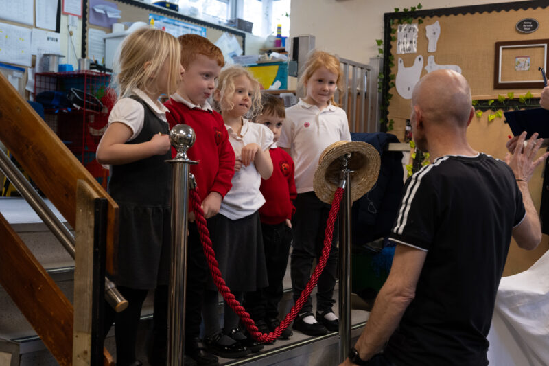 Man kneeling down talking to a group of young children.