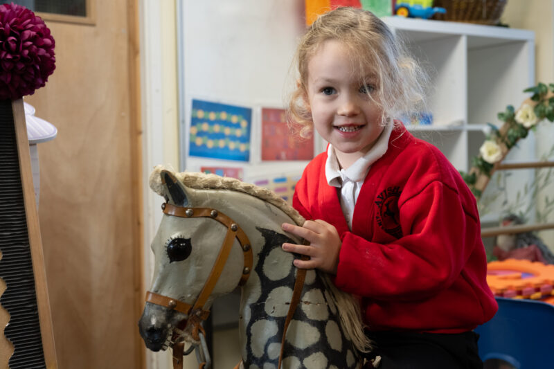 Child smiling at camera riding a vintage rocking horse.