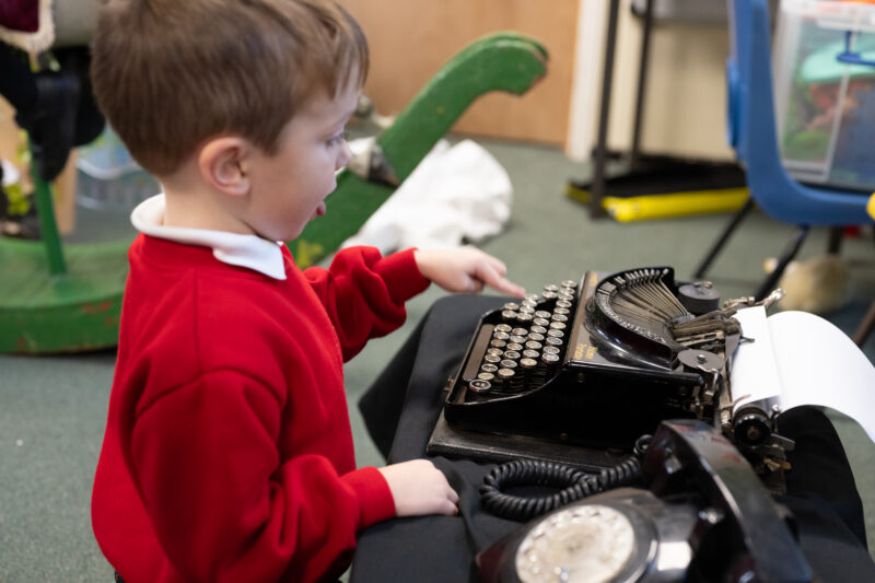 View from side of child playing with vintage typewriter.
