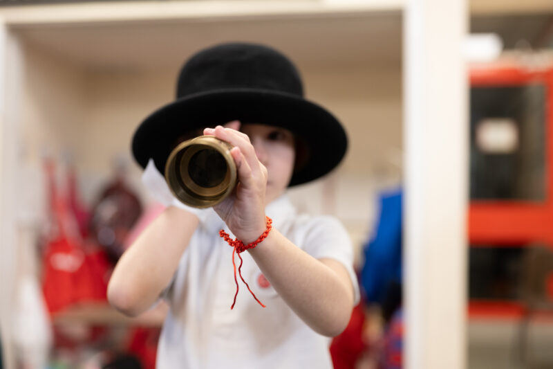 Child wearing a hat looking through telescope at camera.