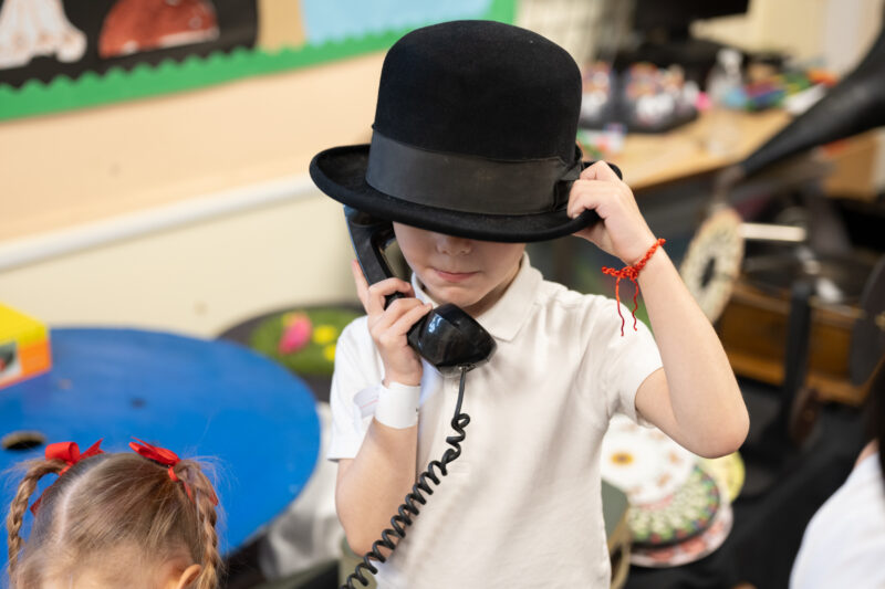 Child wearing a hat speaking into vintage telephone.