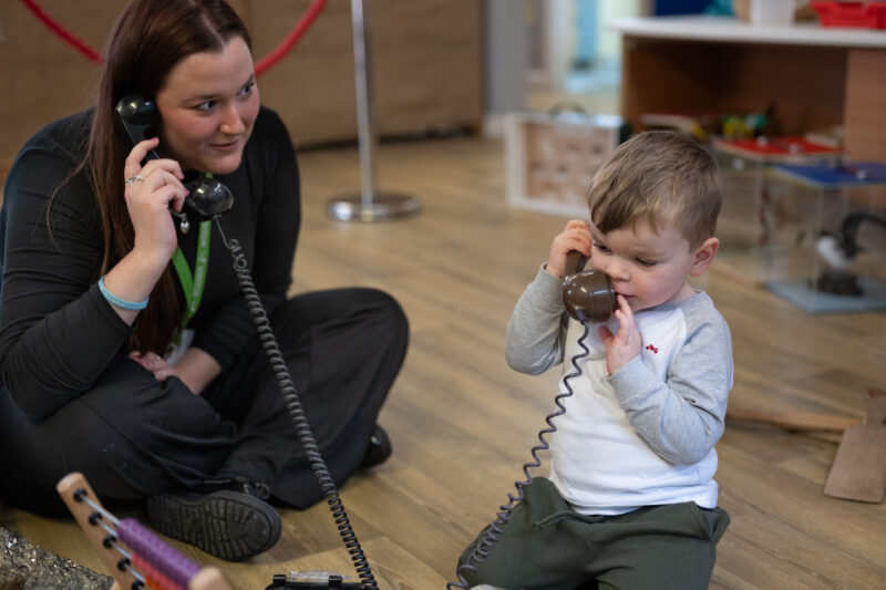 Adult and child pretending to talk to eachother through vintage telephones.