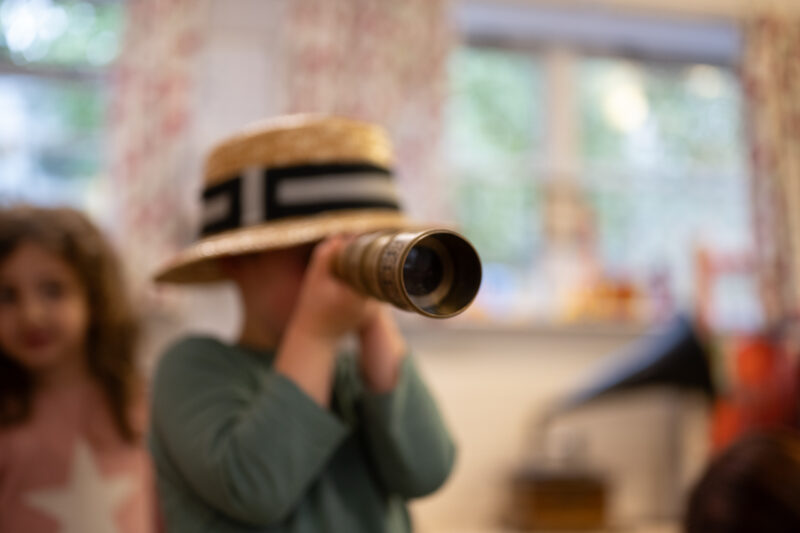 Child wearing a hat looking through a telescope.