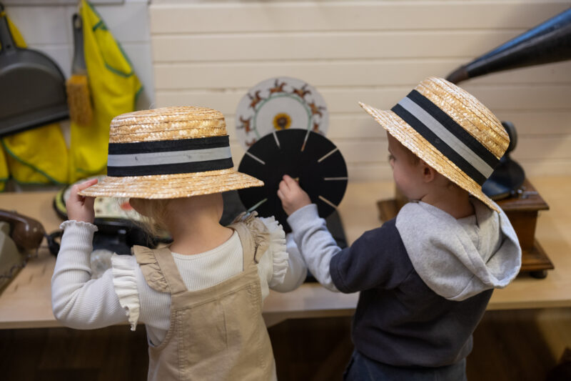 Two children wearing hates playing with the vintage objects (photographed from behind).