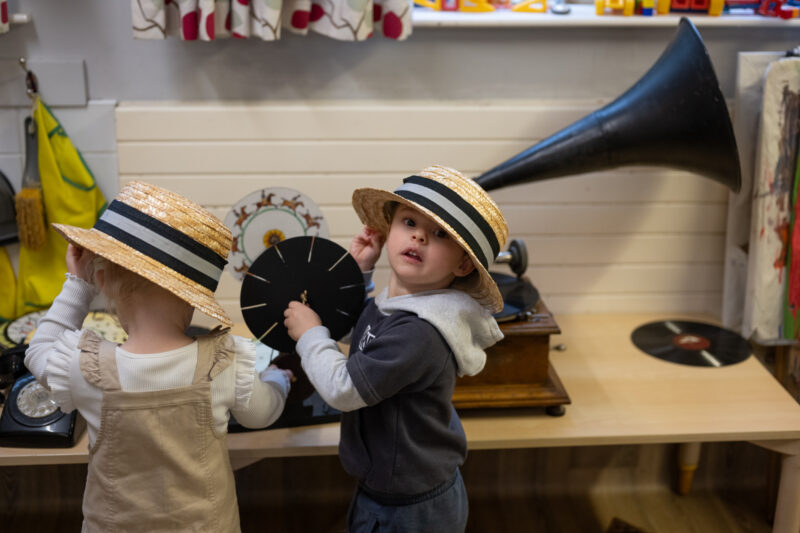 Two children wearing hates playing with the vintage objects (photographed from behind).