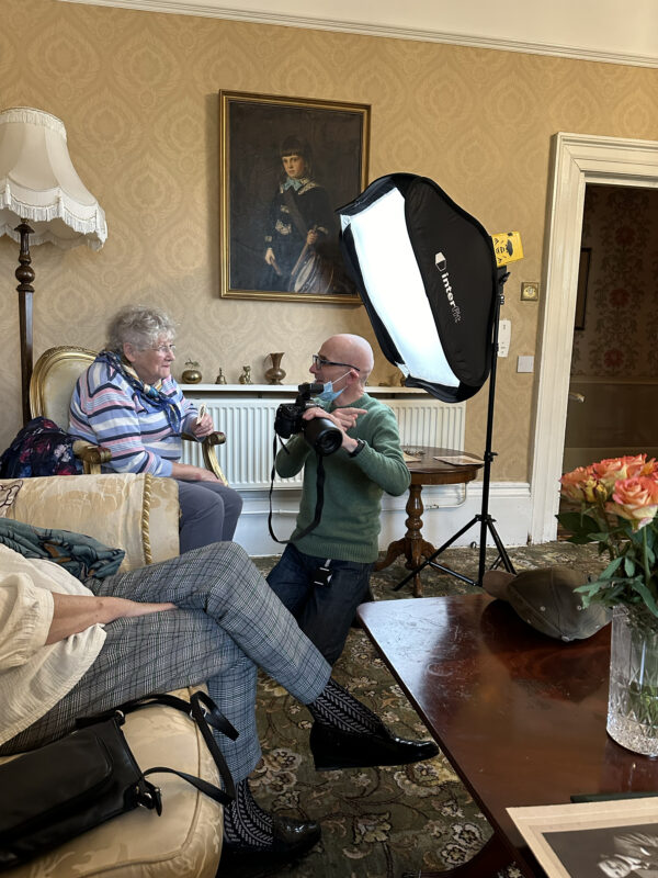 Man kneeling in front of woman, discussing camera set up for a portrait.