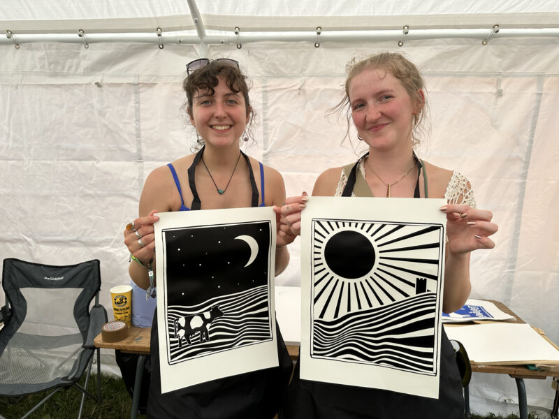 Two people holding up their artwork to the camera.