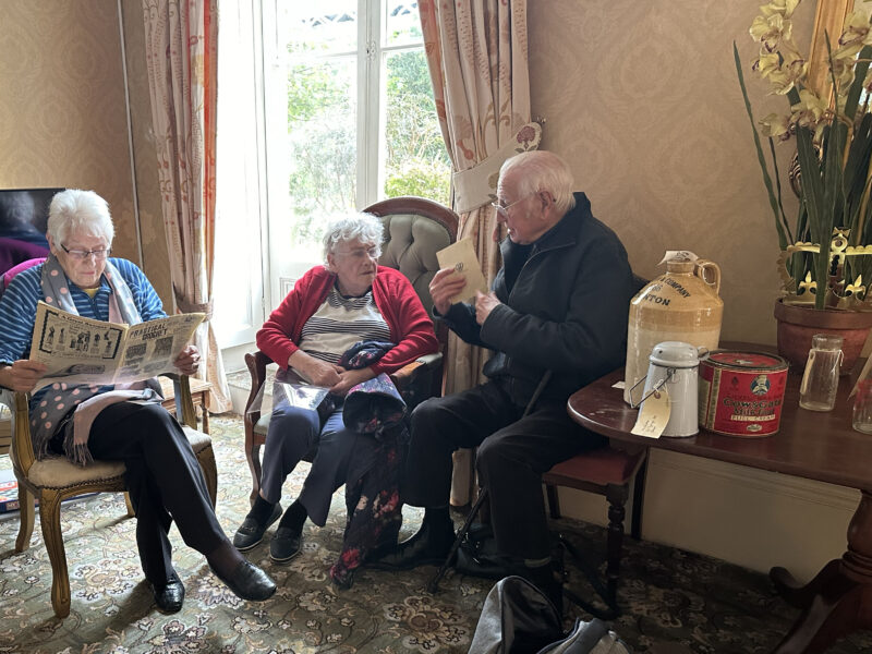 Elderly people gathered around looking at vintage objects.