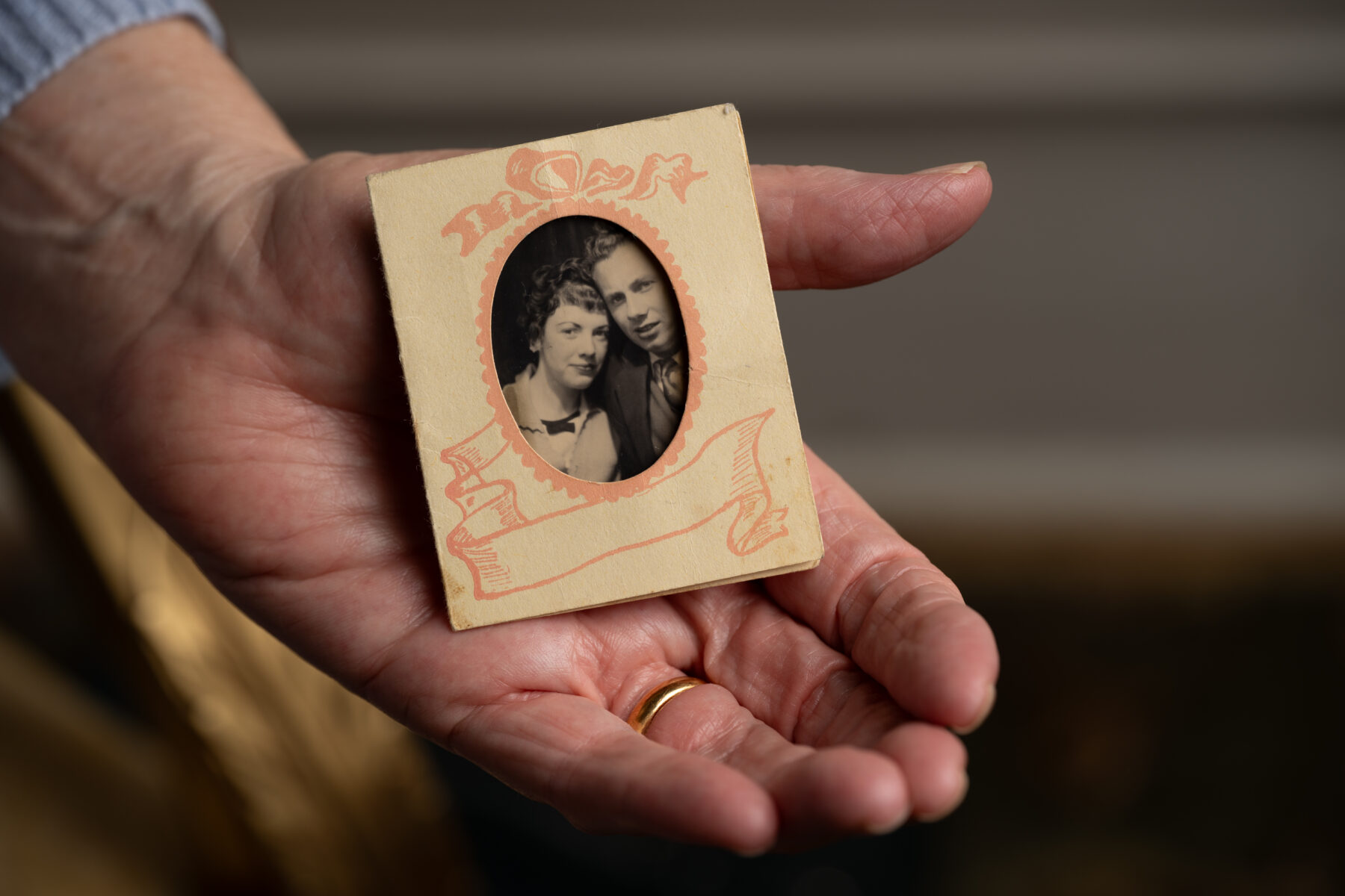 Close up photograph of a woman's hand holding a tiny, old photograph of a couple.
