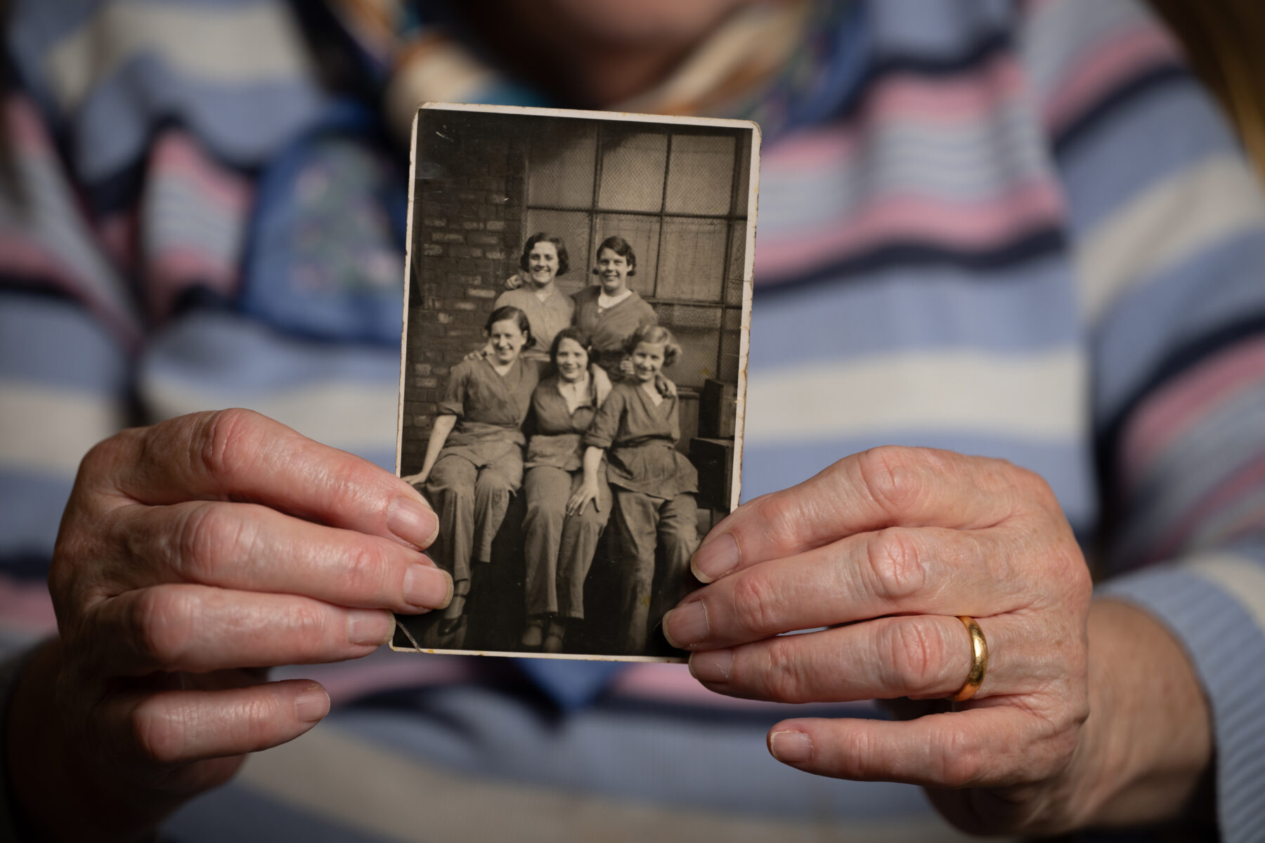An elderly woman holding a small photograph of a group of women from her younger days to the camera.