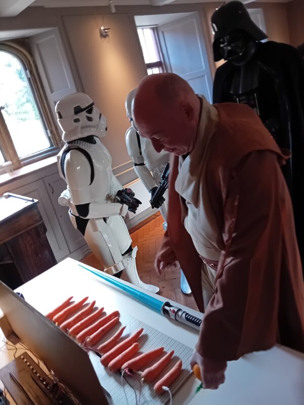 Someone dressed up as a Star Wars character playing a piano made of electrical circuits and carrots.