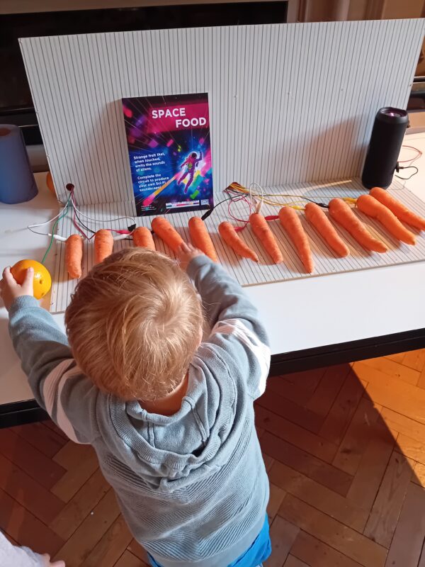A child playing a piano made of electrical circuits and carrots.