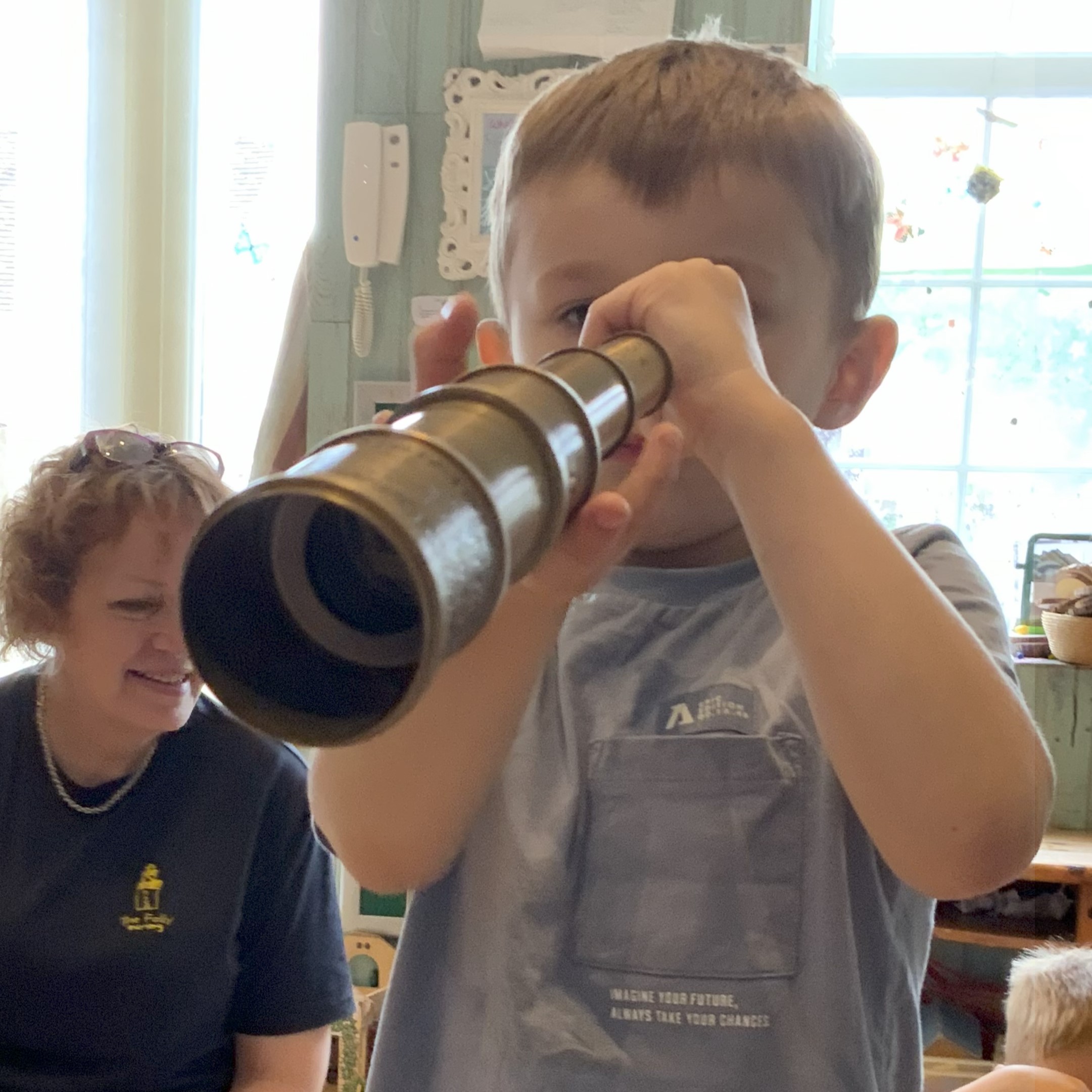 Small child looking through a telescope at the camera.