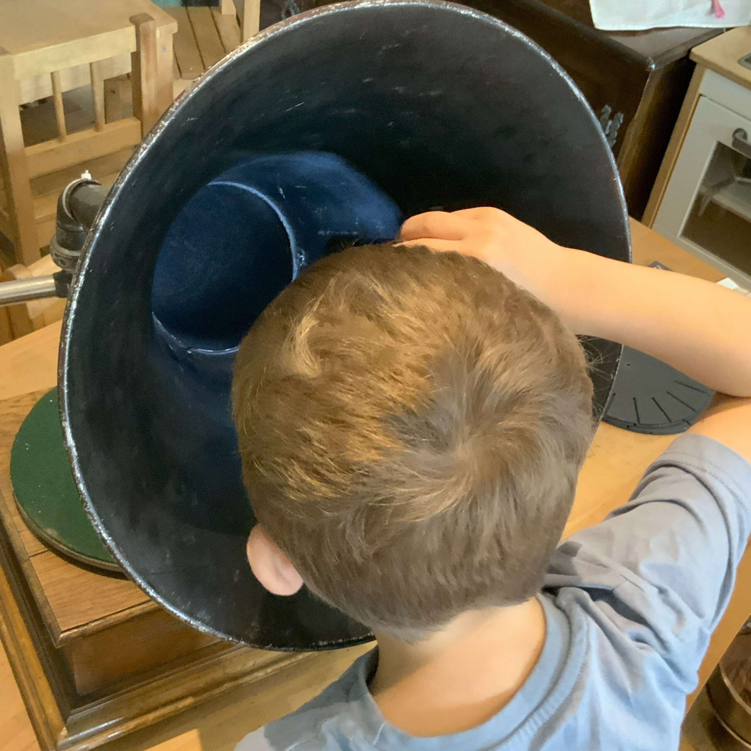 Small child photographed from behind, looking down into the top of a gramophone.