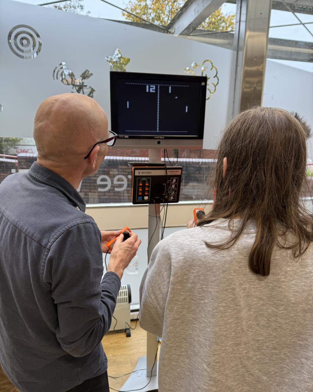 Two people facing away from the camera, playing a vintage games console.