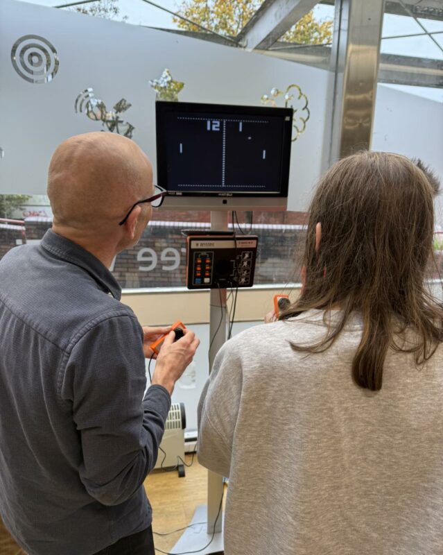 Two people facing away from the camera, playing on a vintage games console.