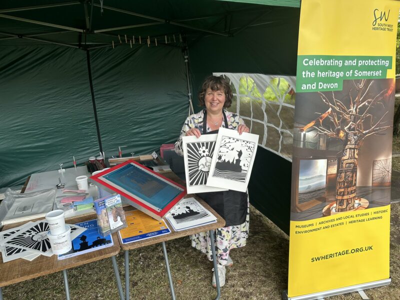 Woman stood under a gazebo holding two printed artworks.