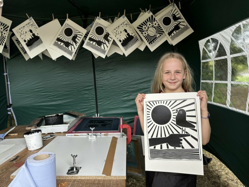 Child stood under a gazebo holding an artwork.