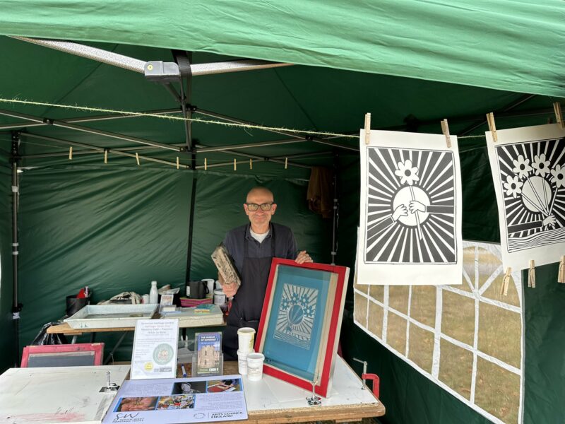 Man holding screen printing equipment under a gazebo.