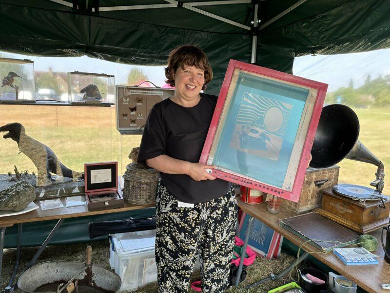 Woman holding screen printing equipment under a gazebo.