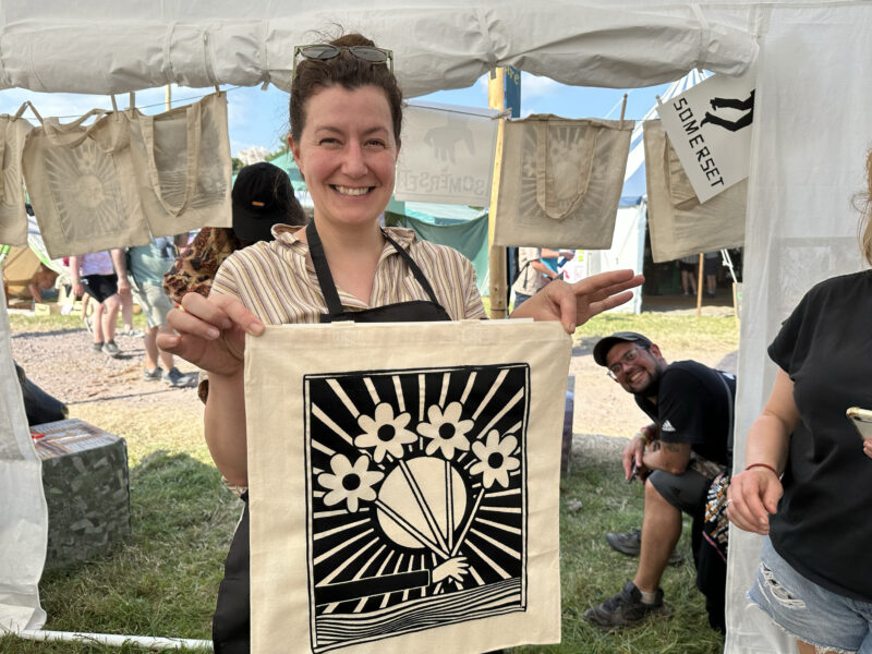 Woman holding up a tote bag with a printed artwork on it.
