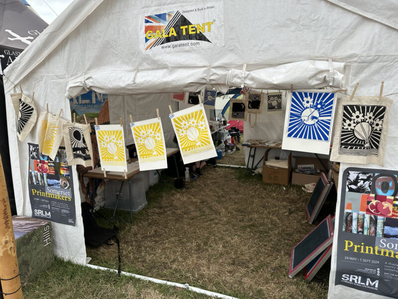 A marquee with artwork hanging from the front, in a field.