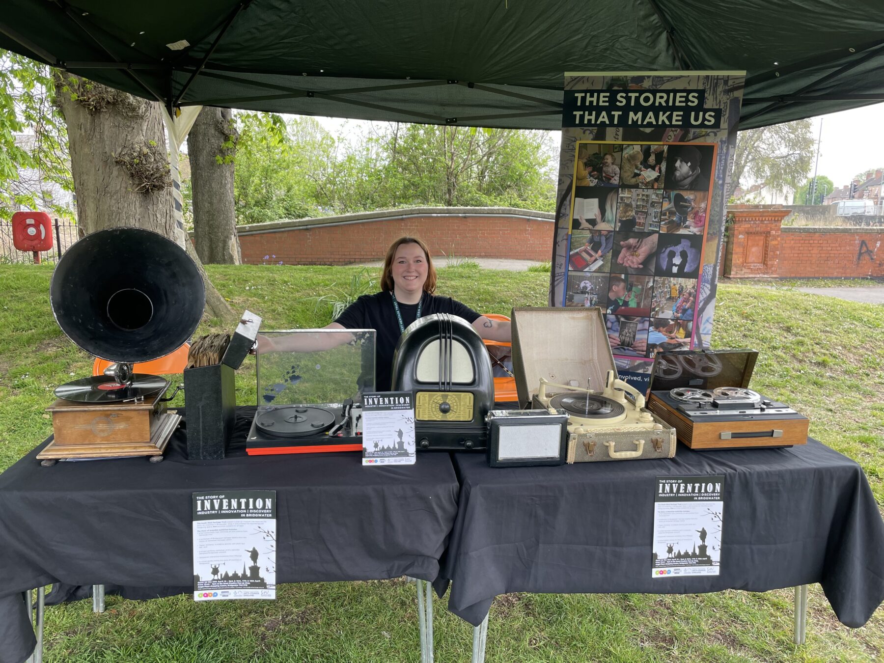 Woman with her arms spread out over a table to show a collection of vintage music players.