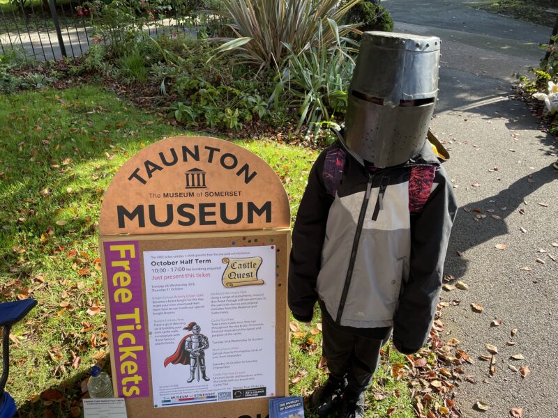 A child dressed as a knight stood next to a museum sign.