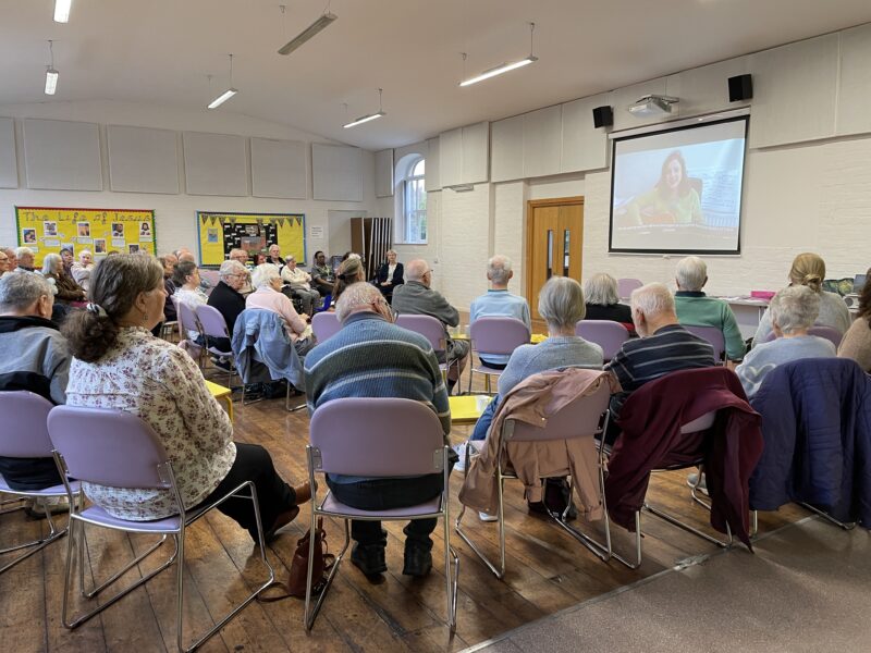 Elderly people sat on chairs in a circle, watching a presentation.