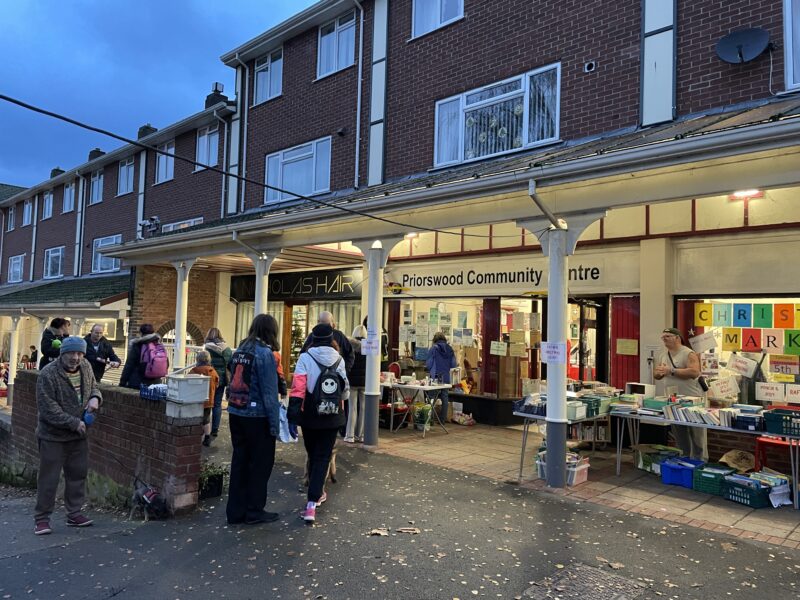 Small crowd of people stood in front of a community center in the dark.