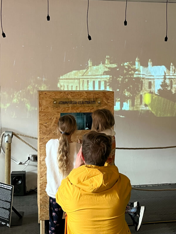 Three people facing away from the camera, looking into an installation.