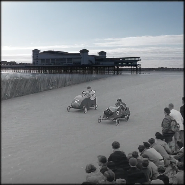 Black and white image of boys racing homemade cars on the beach, overlaid on an image of Weston-super-Mare pier.