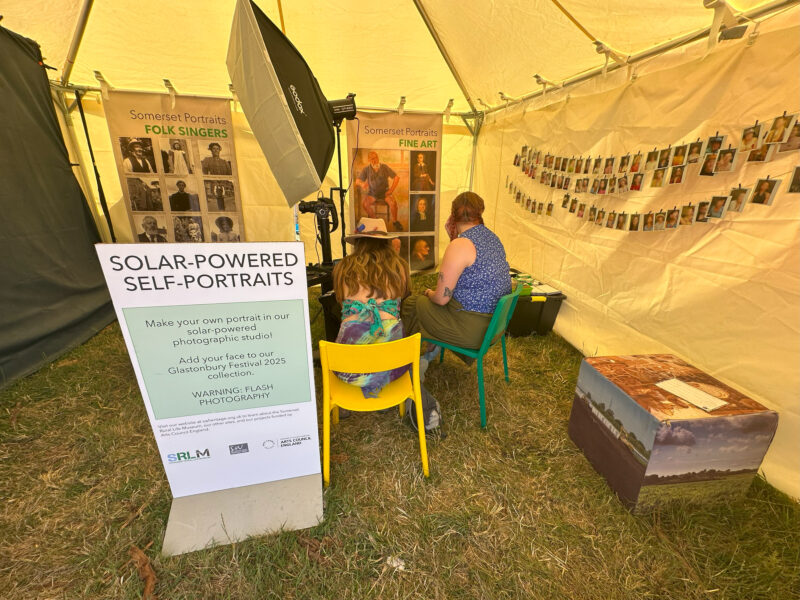 One person sat inside a temporary photographic studio in a marquee in a field.