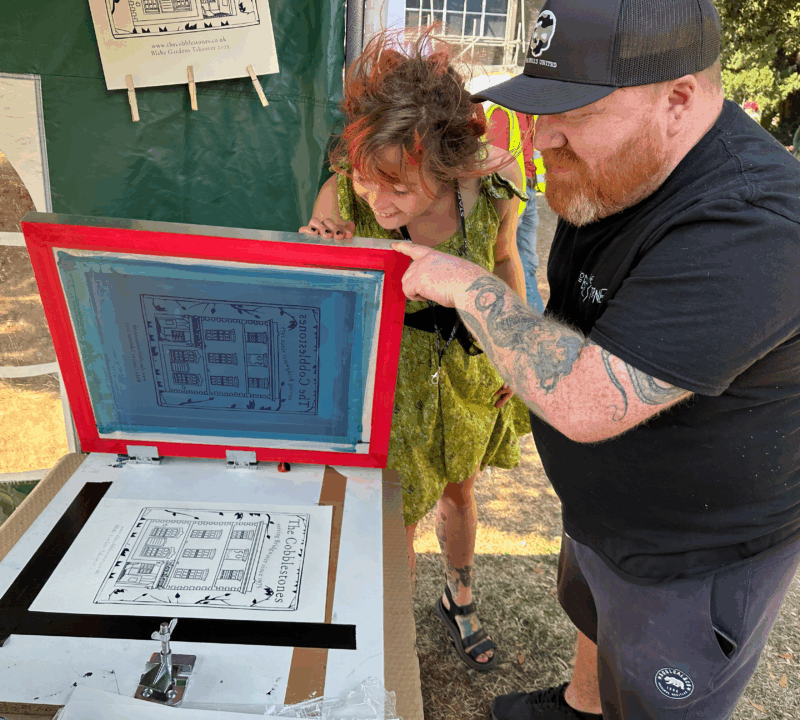 Two people lifting the screen to reveal their print underneath.