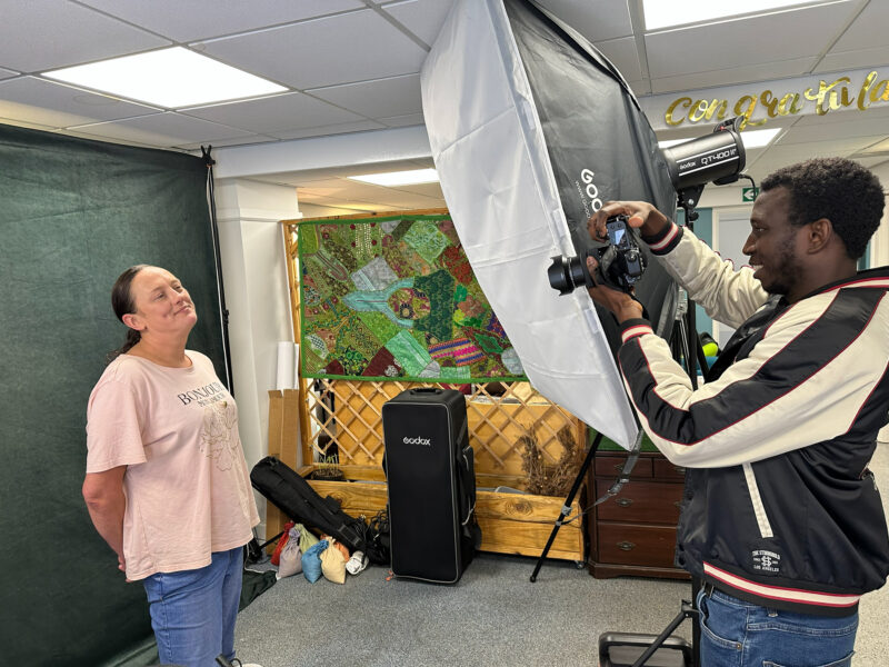 Young man taking a photo of a woman in a pop-up studio, with fabric artwork in the background.