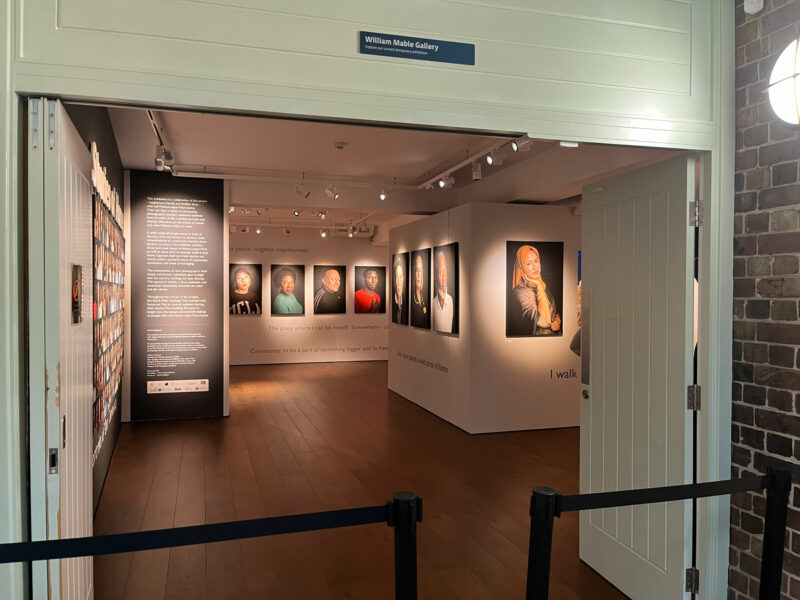 Photo of a gallery space with large portraits on the walls, with a barrier across the doorway.