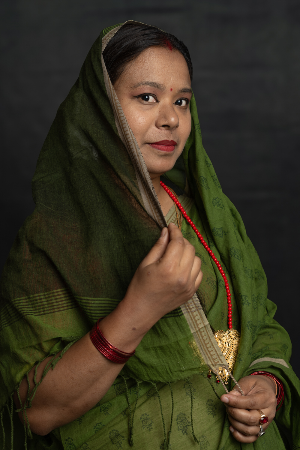 A photographic portrait of a woman of South Asian descent. She has dark hair, is wearing a green outfit featuring a head scarf, and has a red bindi.