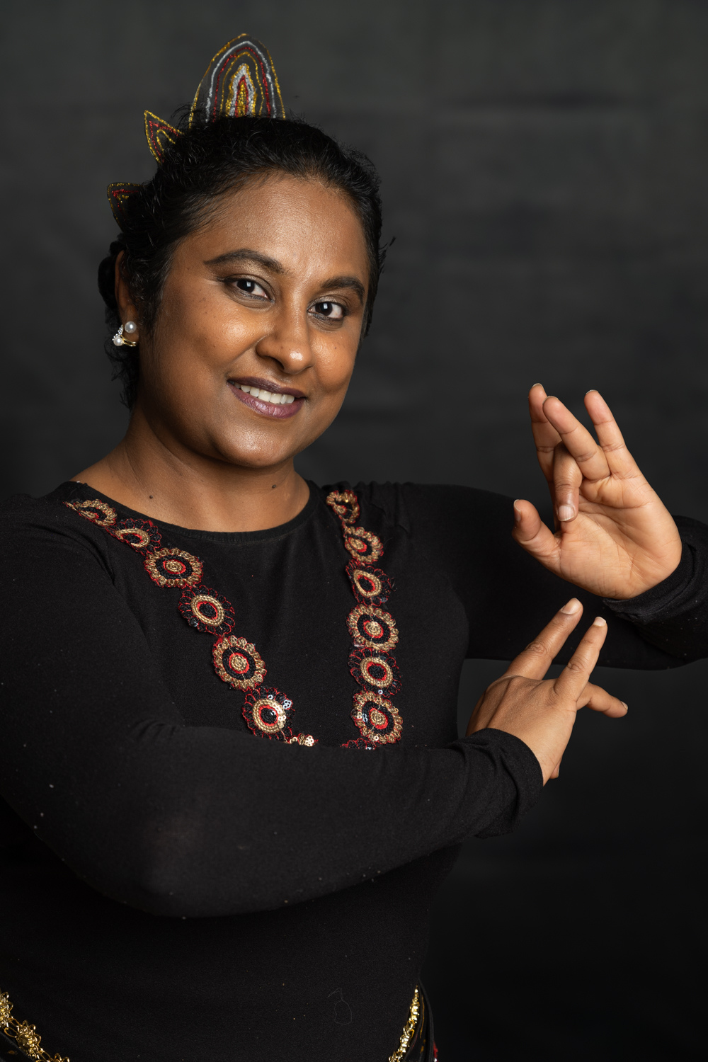 A photographic portrait of a woman posing with her hands by her side. She is wearing a hair accessory and necklace as part of cultural dress.