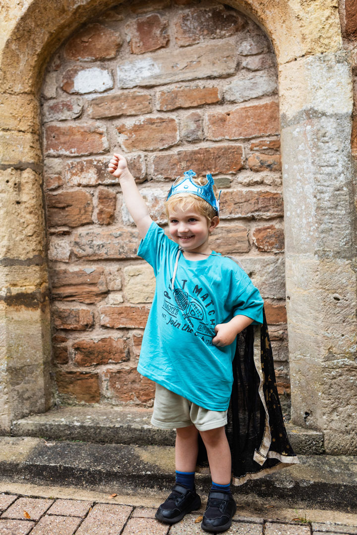A young boy wearing blue, dressed in a crown and cloak.