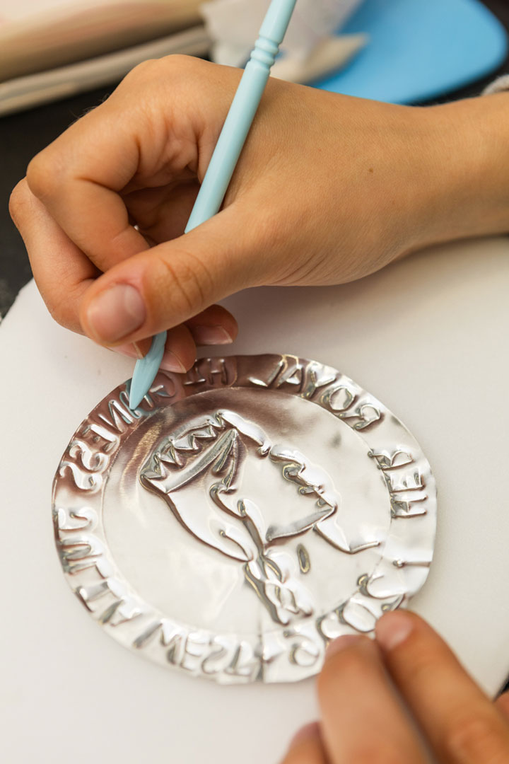 Close up photograph of a participant etching into a foil coin using a blue stylus.