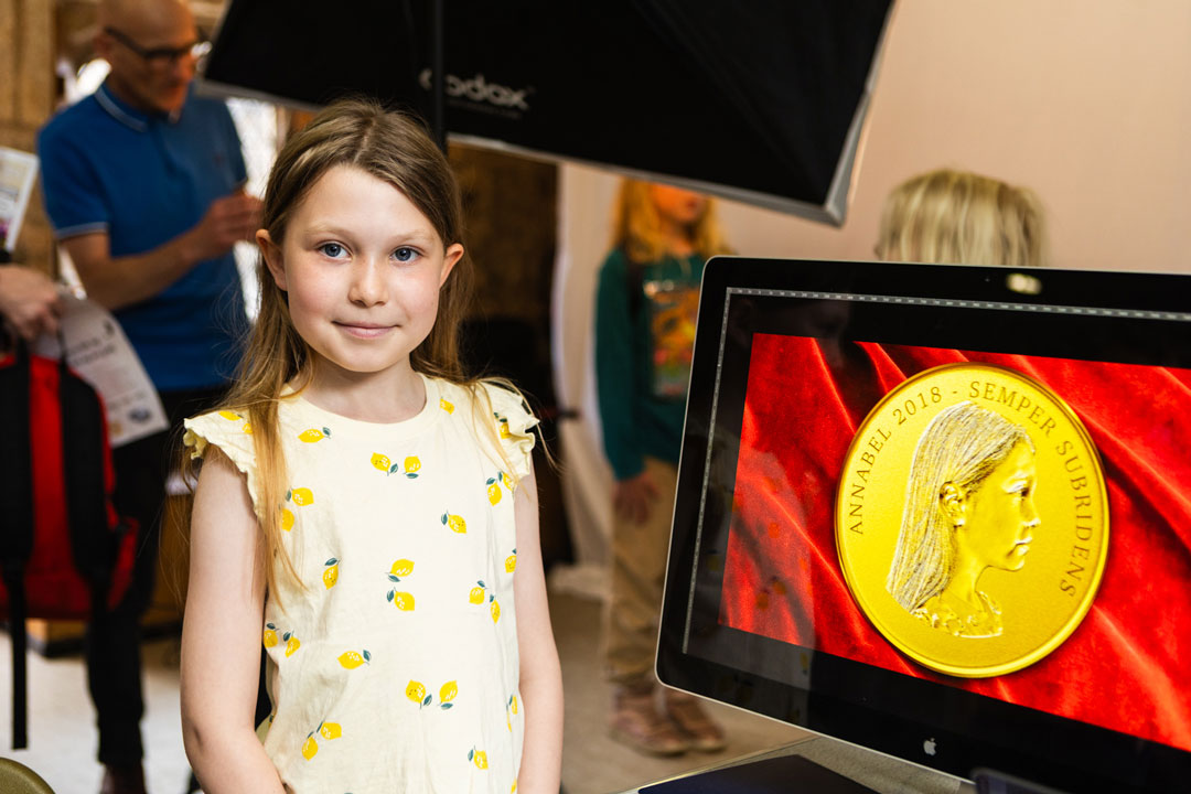 A young girl stood next to a monitor displaying a golden coin version of her side profile.