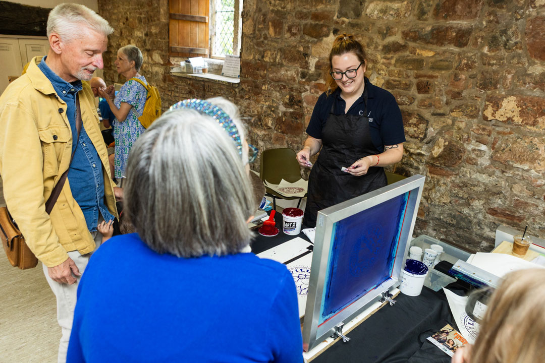 A man and a woman taking part in a screenprinting activity with support from a team member.
