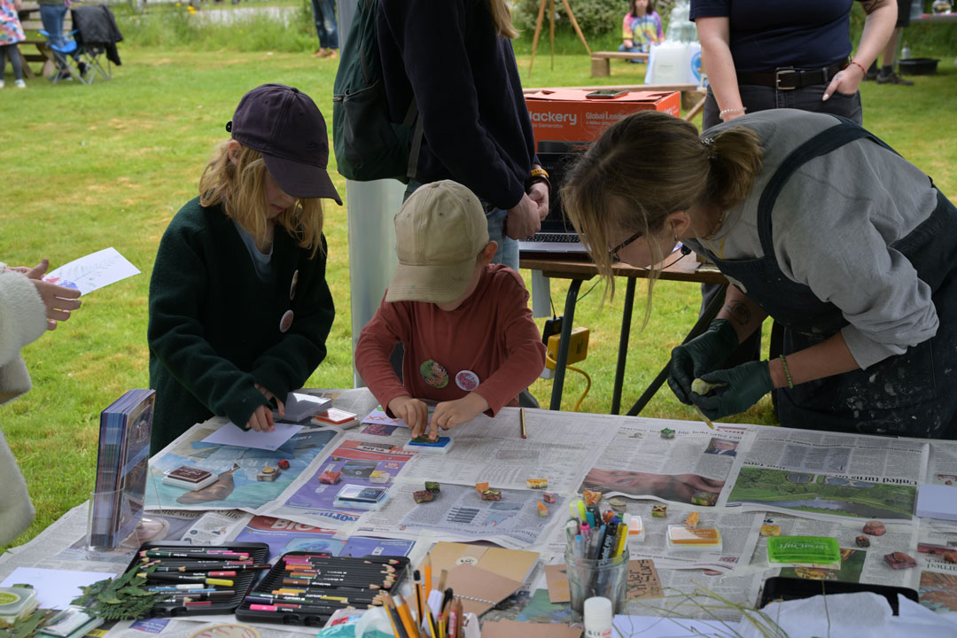 A woman and two small children wearing caps, standing over a table using ink stamps to create artwork.